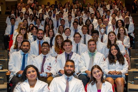 Students wearing short white coats sitting in rows of seats in an auditorium.