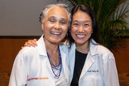 Two women faculty members pose for a photo in an auditorium.